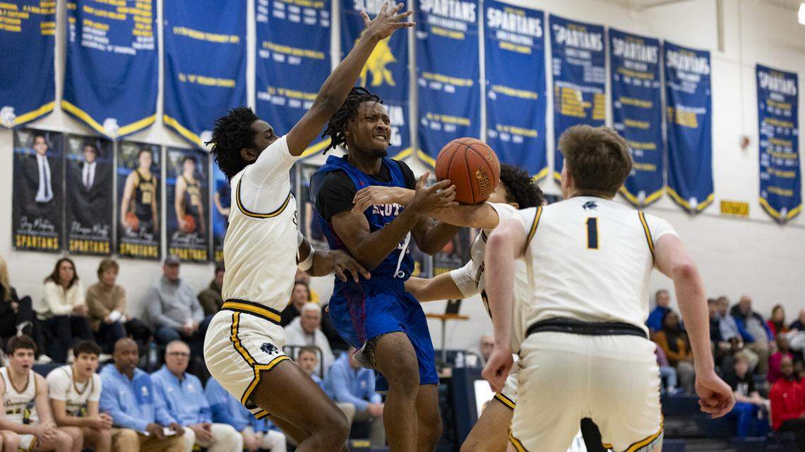 Scott County’s Montae Washburn, center, is fouled on his way to the basket between Sayre defenders Sayvion Staley, left, Kenji Berger and John Gaines, right) during the Cardinals’ 70-39 win at Sayre on Tuesday.