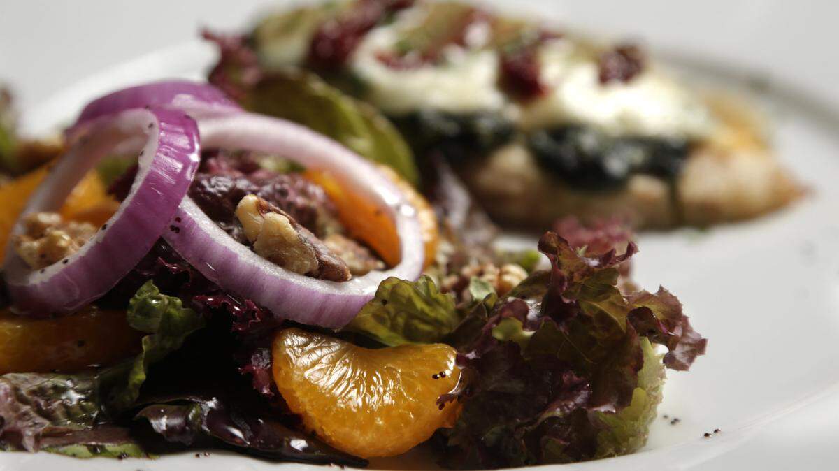 The side salad for the Chicken Fontina di Lucca contains red leaf lettuce, mandarin oranges, rings of purple onion and English walnuts, and is topped with poppy seed dressing.