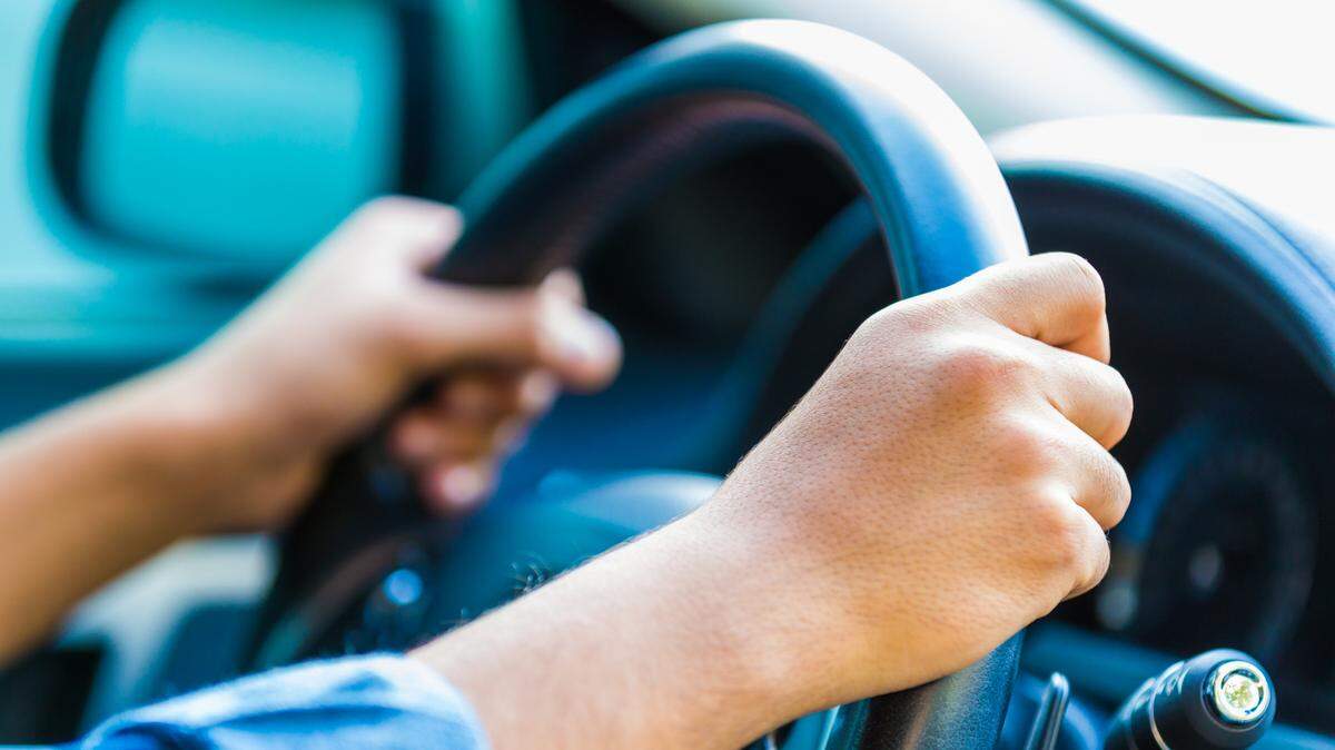 This stock image from GettyImages shows a young man inside his car, only his hands are visible.