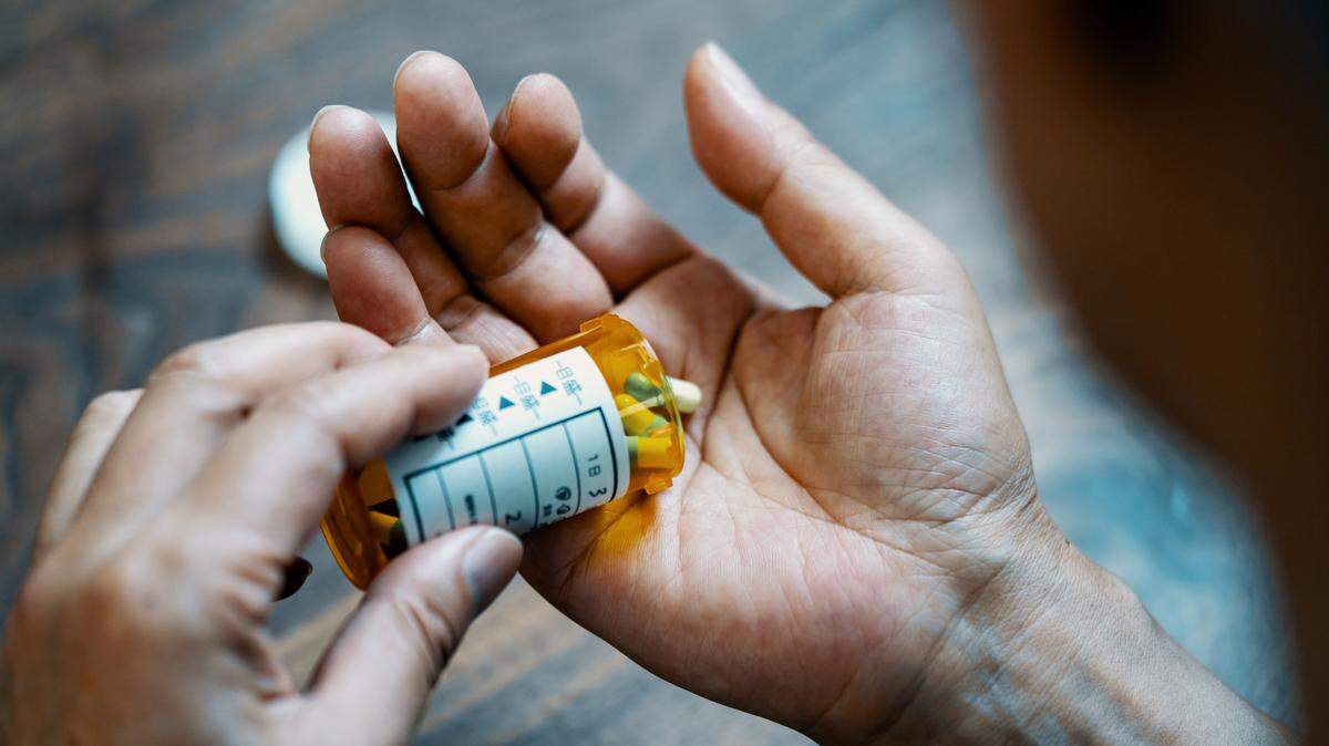 Close-up of a male hand holding a pill bottle pouring medication into his hand in his house