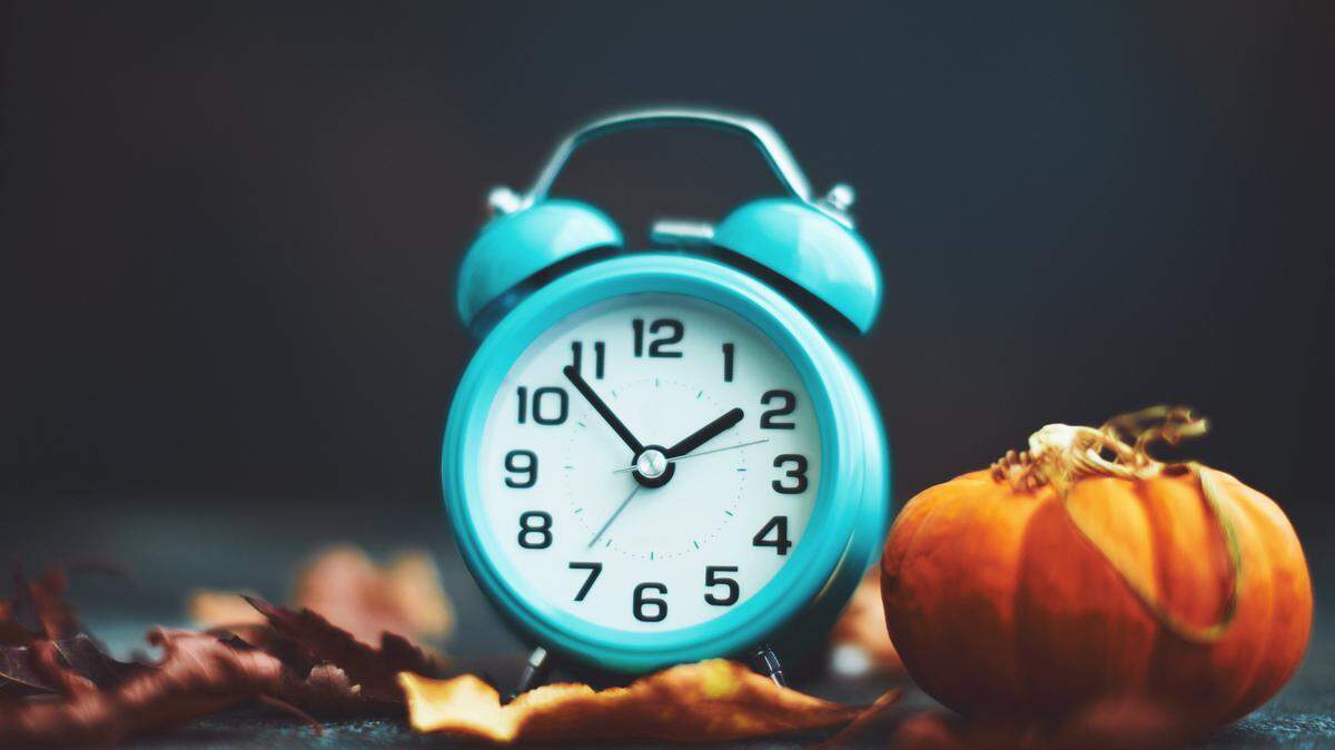 The stock image shows a teal alarm clock with fall decorations for daylight saving time.