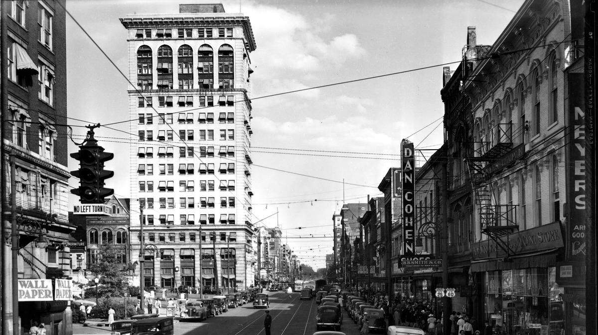 Main Street, downtown Lexington, circa summer 1938. Rails run down the street, but around this time streetcar service was discontinued in Lexington. Like most American cities, as roads were improved and more people bought automobiles, trolley tracks were pulled up or paved over. Motor buses took over the steadily declining demand for public transportation. In the lower left corner of the picture you can see two women and a child waiting for the bus that coming towards them. Along the left side is what is now Henry A. Tandy Centennial Park. Further down is Lexington’s first skyscraper, the First National Building. Built in 1913, it is now a 21c Museum Hotel. The buildings on the right include a Woolworth five-and-dime store and clothing store B.B. Smith & Co., whose sign said it was “Correct Appareral for Women & Misses”. This is now the site of the Lexington Financial Center, or more commonly known as the “Big Blue Building”.