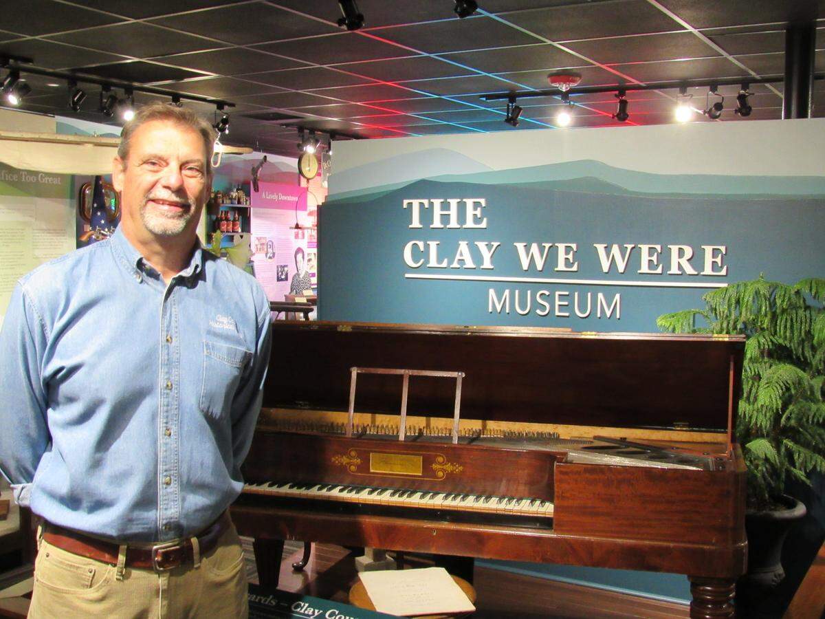 Mike White is president of the Clay County Historical and Genealogical Society, which has won awards for its work. He is shown here with a piano made in the early 1800s that a prominent local family owned.