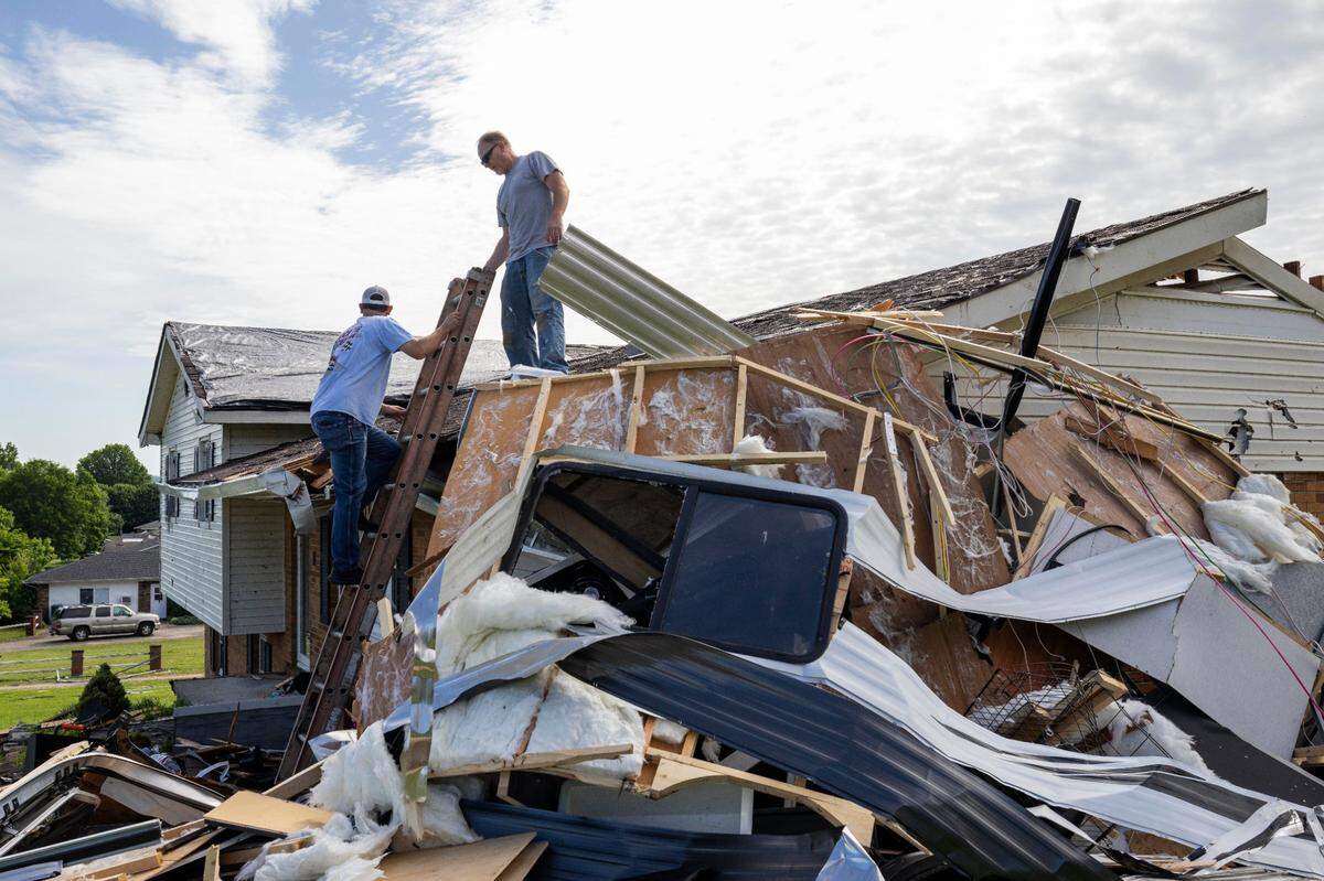 Chris Colier, right, holds the step ladder for John McKinney, who climbs off the roof to grab more tarps on Sunday, May 18, 2025, at his house off U.S. Route 27 in Somerset, Ky.