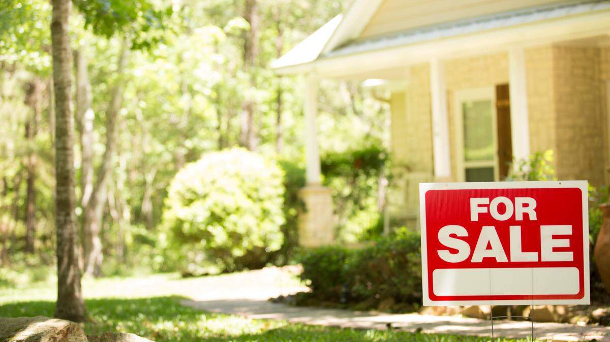 In this stock image, a "for sale" sign stands outside a home on the market. It's sometime in the spring or summer.