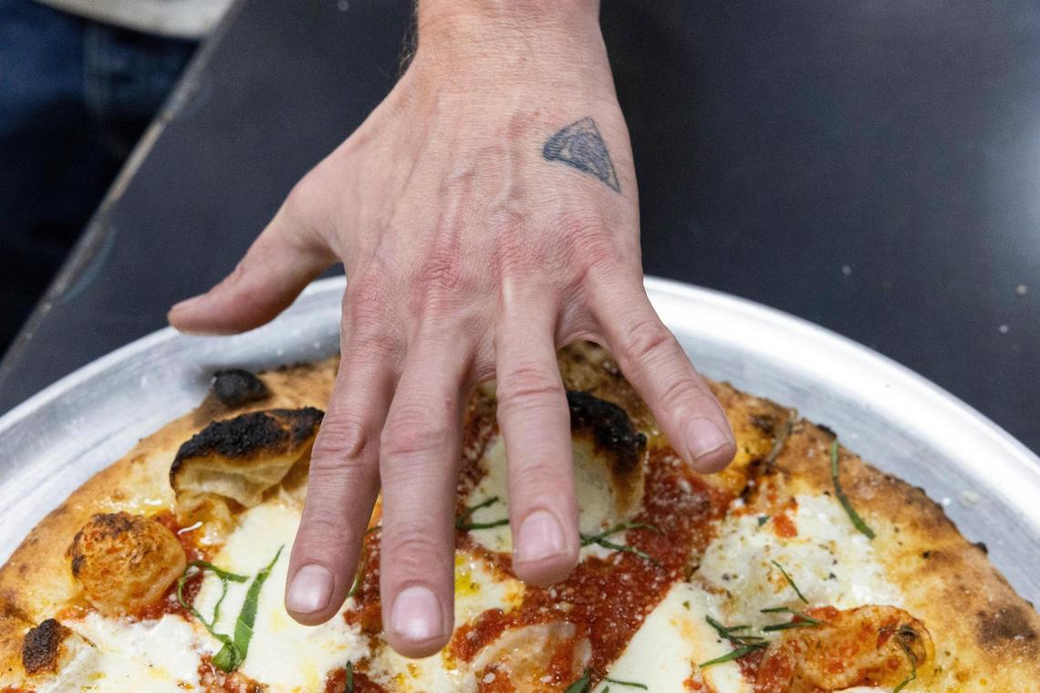 Ethereal Slice House owner Greg Spaulding shows a small slice of pizza tattoo on his hand over a margarita pizza.