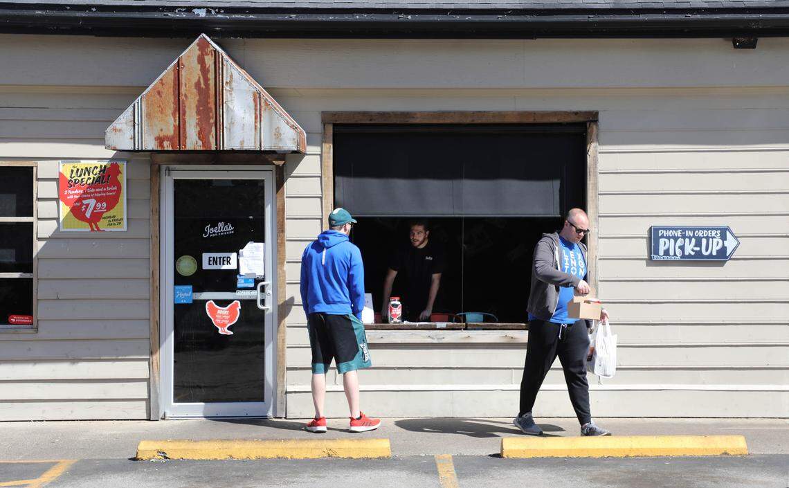 Eric Schneider, right, walks away with a carryout order from Joellas Hot Chicken. The restaurant only takes online payment and orders and has locked the front door, instead giving patrons their food through a dining room window.