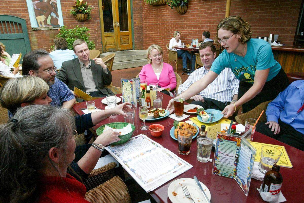 Amber Scott serves a table on Atomic Cafe’s back patio. The Caribbean menu at the Lexington restaurant featured coconut shrimp, jerk chicken, conch fritters, mahi-mahi in banana leaves, ceviche, black beans and rice and spicy cornbread.