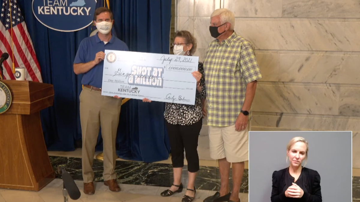 Ginger Schultz of Louisville, middle, stands with Gov. Andy Beshear. Schultz became the second $1 million winner through the Shot at a Million vaccine incentive program on Friday.