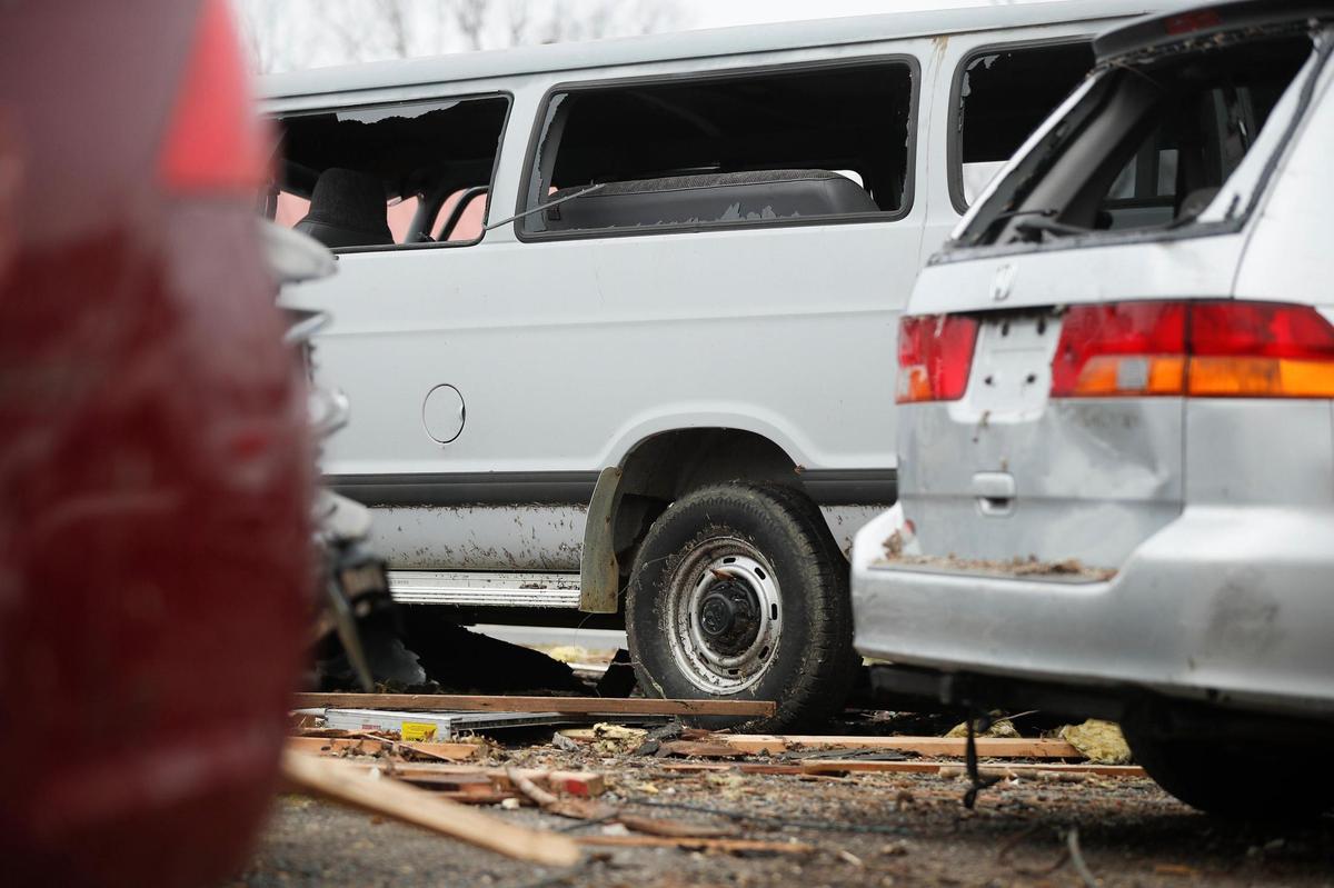 A Dodge Ram passenger van sits damaged along with other vehicles and building debris in a lot along Paducah Road in Mayfield, Ky.