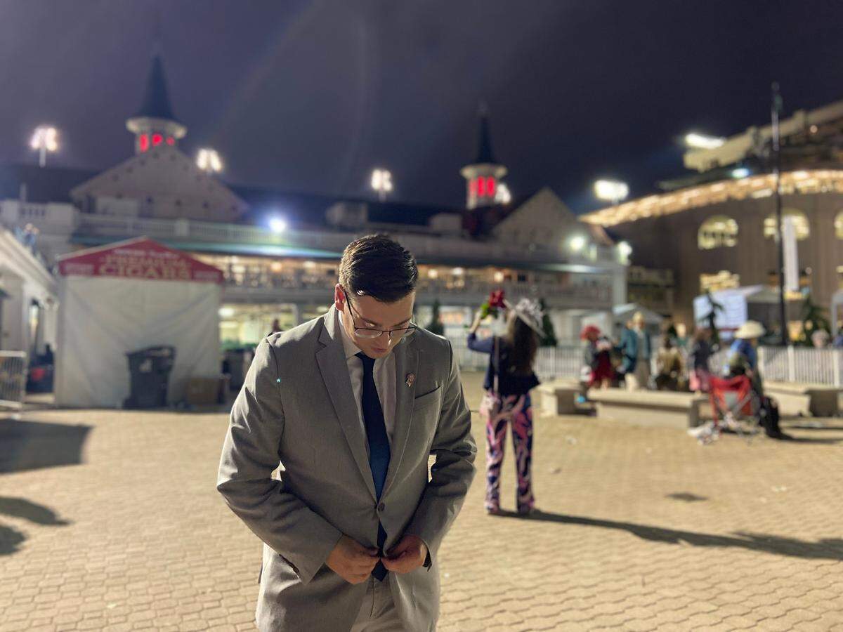 Lexington Herald-Leader sports reporter Cameron Drummond buttons his suit jacket in front of the iconic twin spires at Churchill Downs in Louisville following the 2022 Kentucky Derby. Drummond, who began working at the paper in July, tried his first mint julep on Saturday. He did not like the taste.