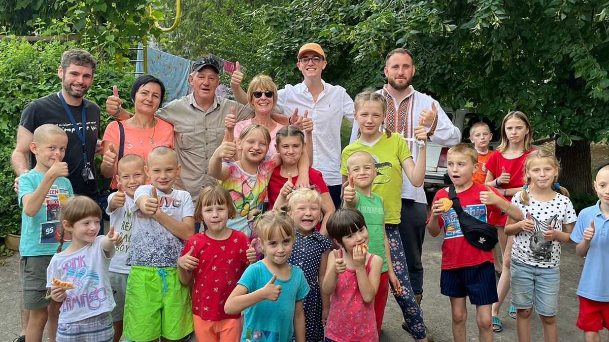 Joan Root of Lexington, wearing sunglasses, has been volunteering in the Ukraine to help families displaced by the war. She is serving Ukrainian families pizza as part of an international volunteer effort in 2023.