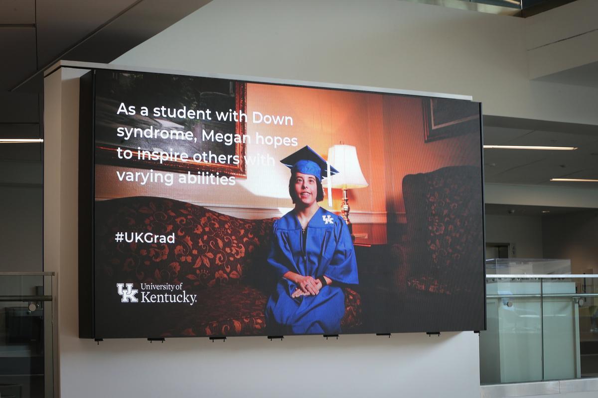 The student center display flashed Megan McCormick, who has Down syndrome and will graduate Friday with a bachelor’s degree in liberal studies from the University of Kentucky, posed for a portrait Tuesday at the UK Student Center. Photo by Matt Goins