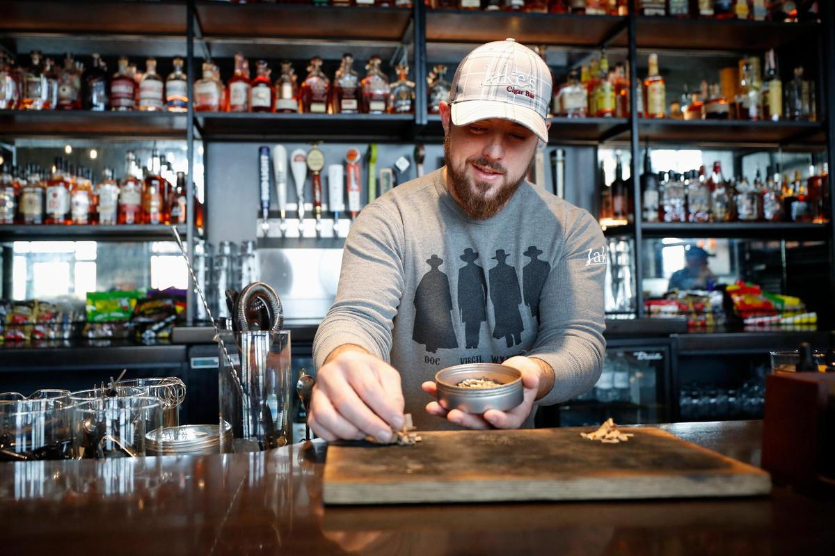 Bartender Cavanaugh Ragone arranges wood chips from a Knob Creek barrel pick Oct. 5 to be used in a Smoked Old Fashioned at Jake’s Cigar Bar. The drink is a popular paring with the bar’s cigars.