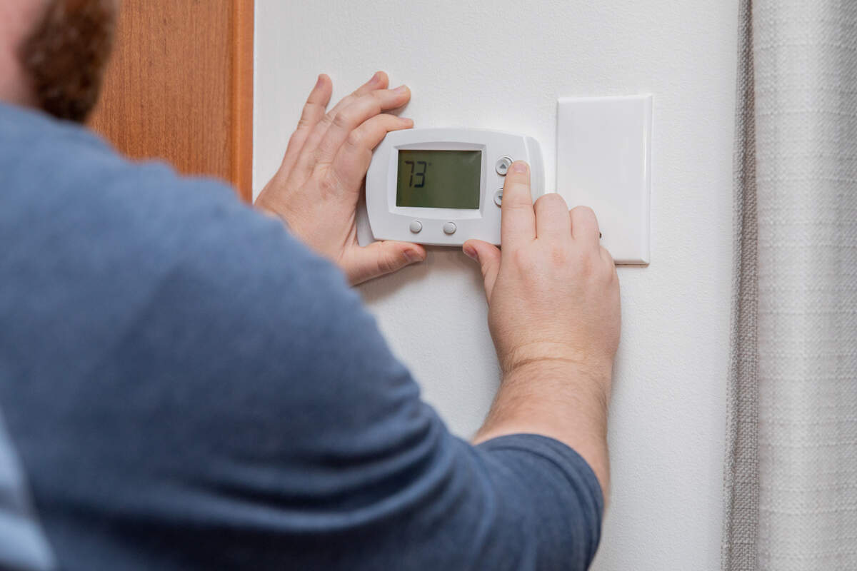A man adjusts a home thermostat.