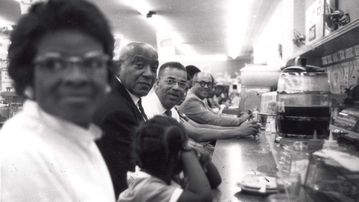 Local ministers at a sit-in demonstration at F.W. Woolworth’s lunch counter in the early 1960’s in downtown Lexington, KY. African Americans were not allowed to eat at the lunch counters in the dime stores and were expected to purchase food and leave or stand at the snack bar. From left: Mary Brandon, Rev. W.H. Howard (pastor of Consolidated Baptist Church), Rev. J.S. Beverly (pastor of Bethel Baptist Church), and Rev. A.B. Lee. Photos of the civil rights movement in Lexington, KY in the 1960’s. Photo Courtesy Calvert McCann. Historical photograph.