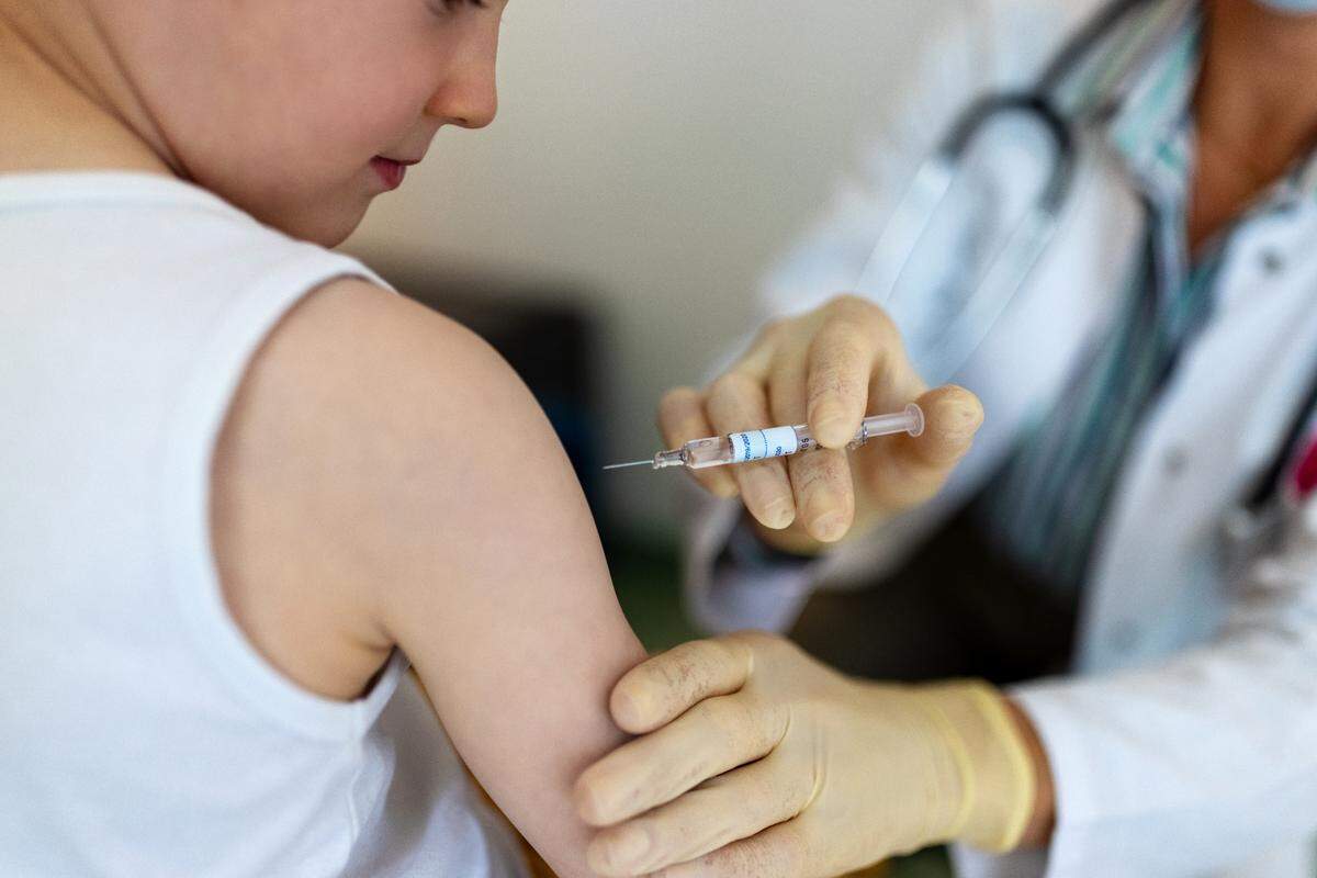 Boy getting a flu vaccine in the clinic. Small boy getting a vaccine on his arm by a pediatrician wearing gloves.