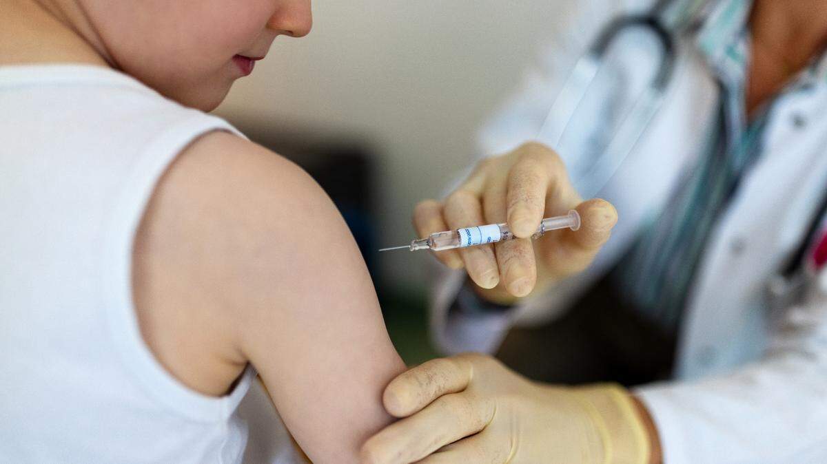 Boy getting a flu vaccine in the clinic. Small boy getting a vaccine on his arm by a pediatrician wearing gloves.