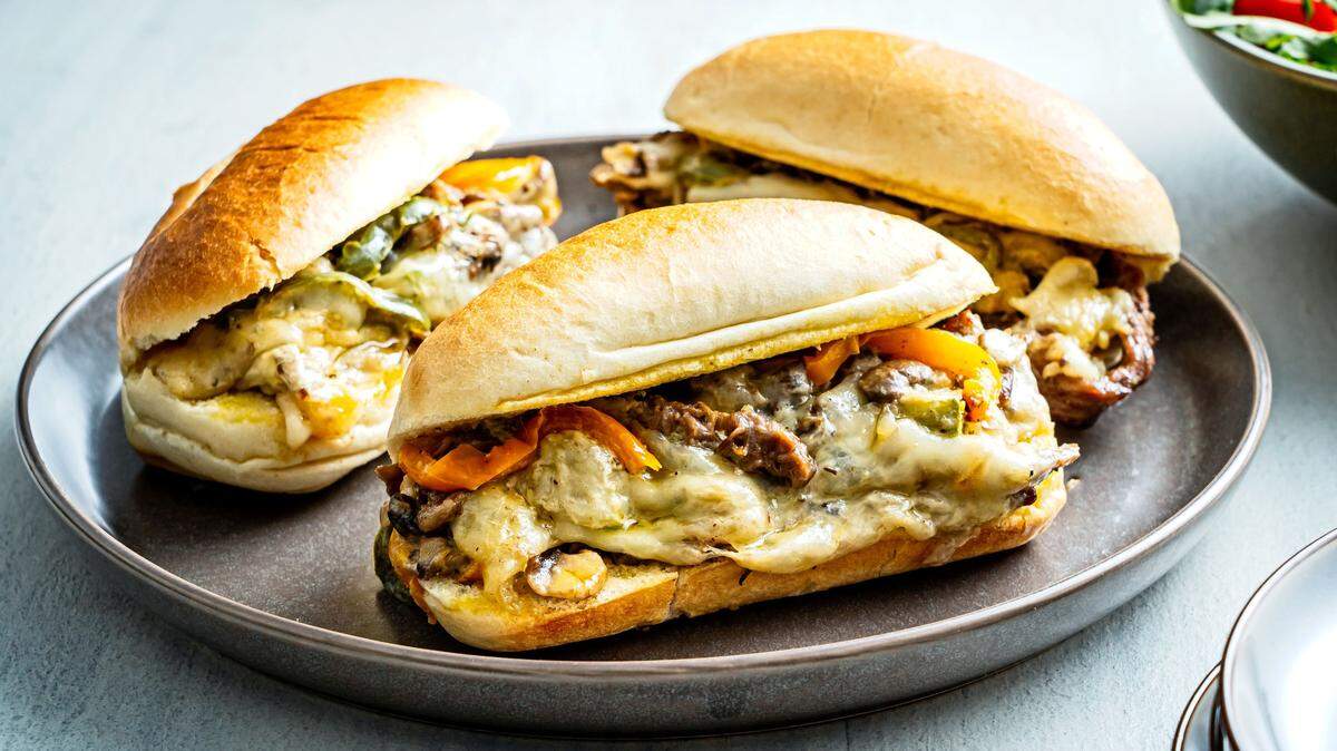 Steak, peppers, mushrooms and creamy, melted cheese are cooked on a rimmed baking sheet for this adaptation of the classic Philadelphia cheesesteak sandwich.
