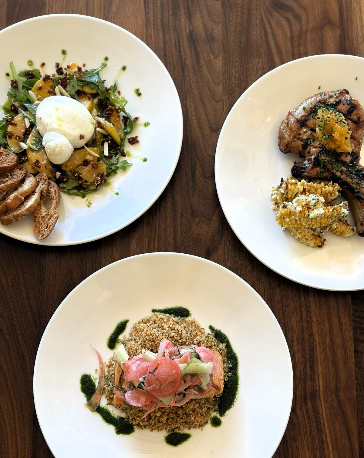 Clockwise from top, new summer menu items at Bella Cafe & Grille include Burrata Al Pesca (thyme sherry marinated peaches, toasted almonds, basil oil, fresh arugula, chili crunch and served with a side of crostinis), Garlic Glazed Pork Chop (served with habanero roasted peach jam, grilled corn ribs with lime aioli and ricotta salata) and Summer Herb Salmon (served with lemongrass basil couscous, fresh cucumber and radish shallot fennel pickled salad).