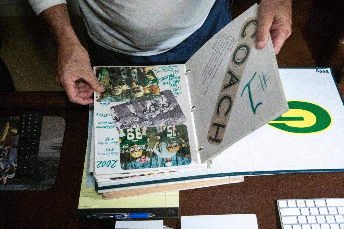 Doug Charles leafed through a scrapbook recalling some of his youth football teams. Players who started with Charles as children often still seek him out for guidance as adults.