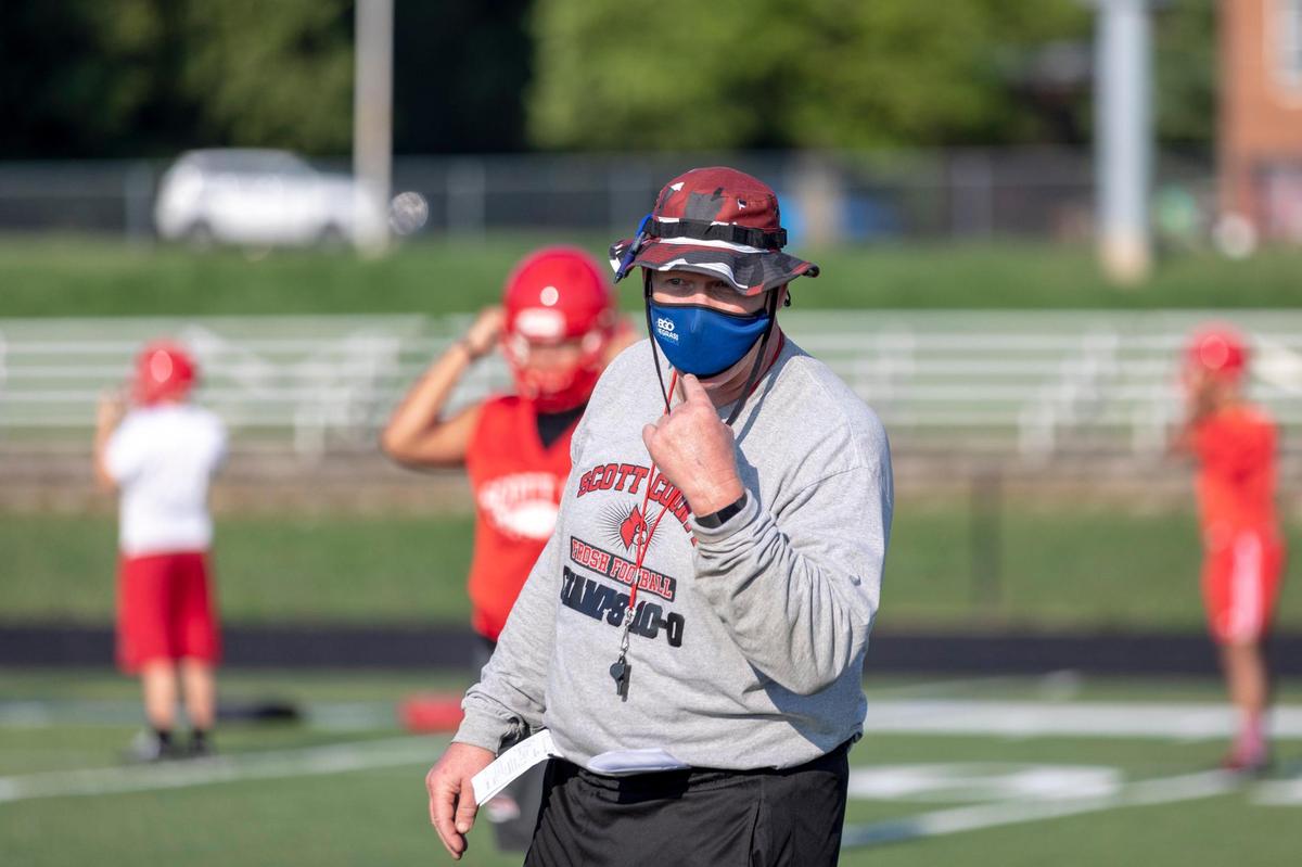 Scott County head coach Jim McKee talked to his players while pointing at his mask during the team’s first practice in helmets on Monday. The coaches wore masks and the players left extra distance in lines during the practice.