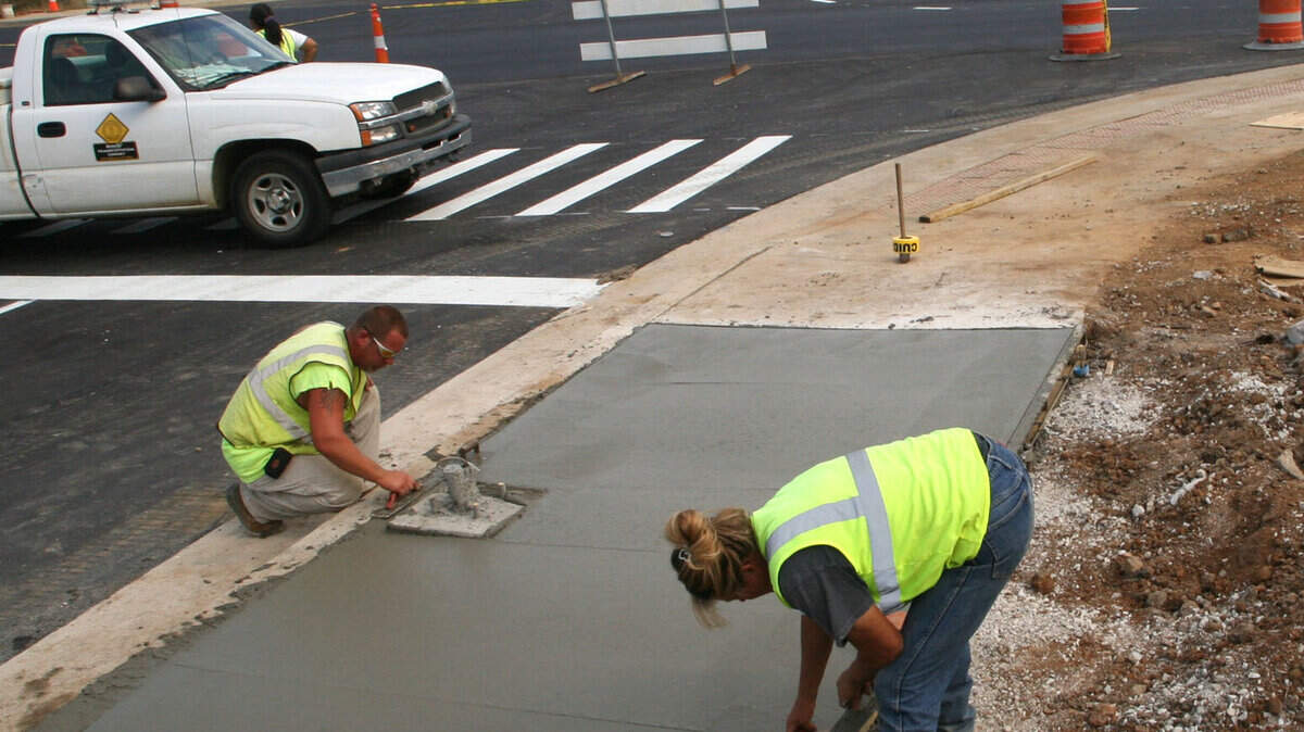 Tommy Willoughby, left, and Katrina Staggs put the finishing touches on a sidewalk ﻿Monday﻿ on the Newtown Pike extension near the Maxwell Street intersection.    