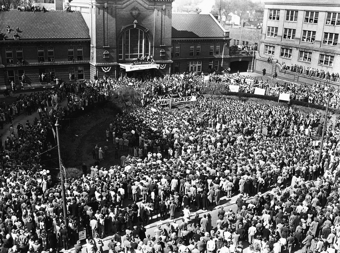 A crowd of 15,000 fans greeted the University of Kentucky’s 1948 NCAA national championship team, April 2, 1948 outside Lexington’s Union Station on Main Street after their arrival from New York. It was the schools’ first NCAA title and the team was met by politicians, three bands and football coach Paul “Bear” Bryant when they stepped of the train. Coach Adolph Rupp and members of the squad were assembled on a platform in front of the door of the station for a brief ceremony. The crowd overflowed all standing room on the ground level around the station, covered building roofs and filled windows furnishing vantage points. Center Alex Groza, the NCAA Tournament’s Most Outstanding Player, was met with a roar of approval after he told the vast crowd, “We said we’d bring home the bacon and we just hope we brought enough.” After the bands played “On, On, U of K,” the team climbed aboard a fire truck for a ride through a decorated downtown Lexington to campus before at least 5,000 more fans.