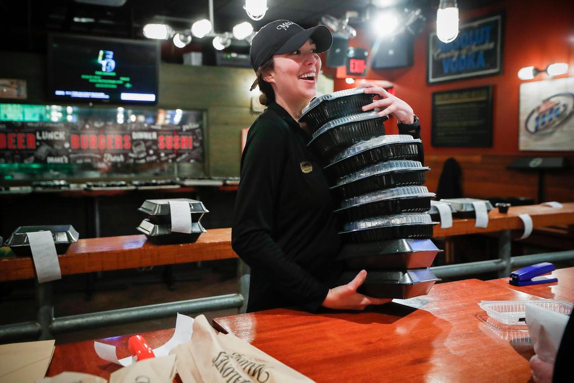 Meredith Johns laughs with a coworker while preparing a takeout order Saturday at Malone’s Lansdowne. The majority of the staff is laid off at the moment because of the dine-in shutdown.
