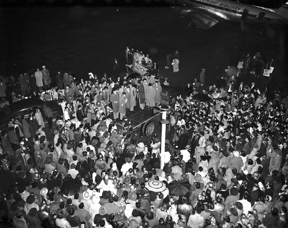 University of Kentucky basketball players were surrounded by a crowd of 1,500 rain-soaked fans and the UK band March 28, 1951 on their return to Blue Grass Field after winning the NCAA National Championship. The Cats beat Kansas State 68-58 the day before in Minneapolis, claiming their third basketball title in four years. After exiting the plane, the team climbed aboard a truck, displaying the trophy. Some Chamber of Commerce officials held a ceremony praising their win and each team member was given gift certificates from a local businessman. The team was then loaded into convertibles, and led by the UK band, marched from the West Main Street viaduct to Rose Street. More than 800 cars, with horns blaring, participated in the parade. Coach Adolph Rupp did not accompany the team home. He stayed in Minneapolis to attend the final sessions of the NCAA coaches convention.