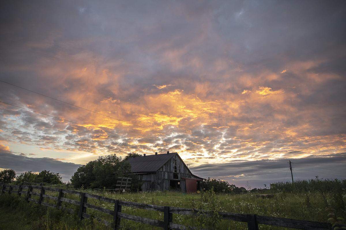 The rising sun illuminates clouds above a barn along Hackett Pike near Richmond in Madison County Tuesday, June 25, 2019.