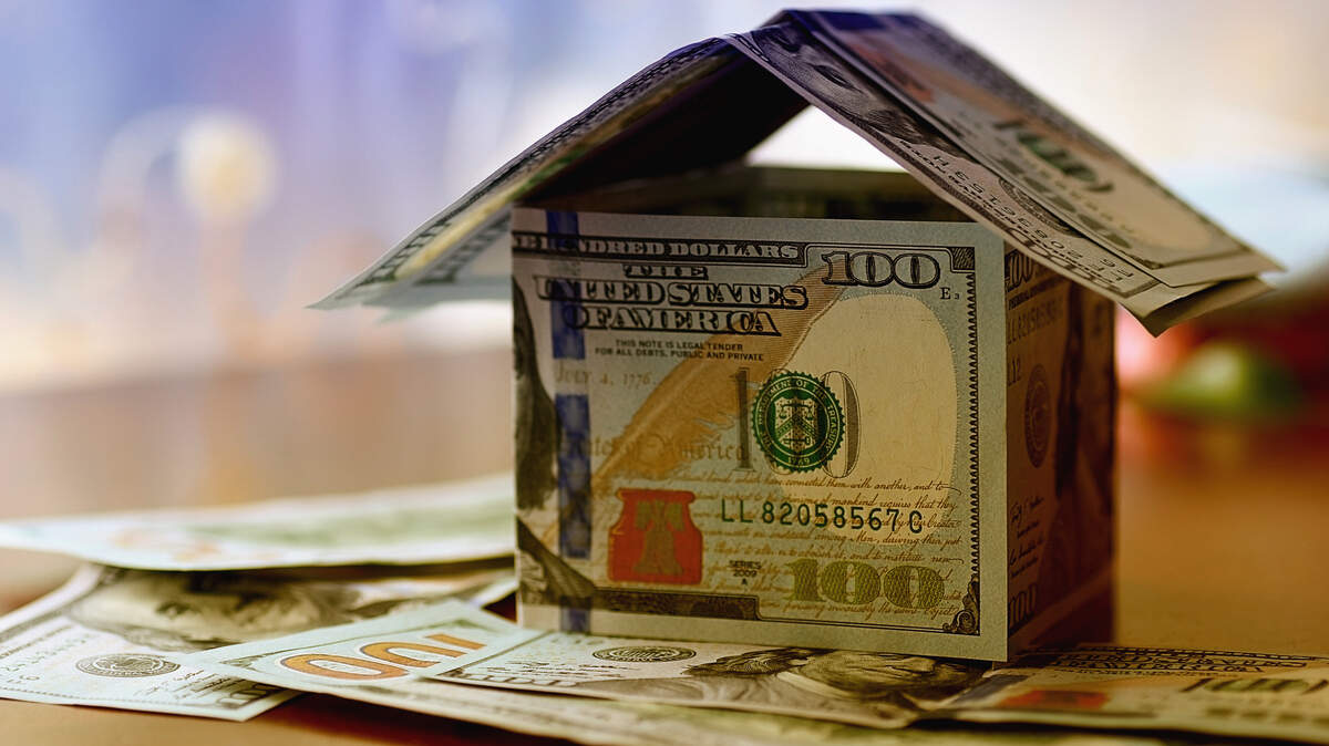 The stock image shows a miniature house made out of $100 dollar bills.