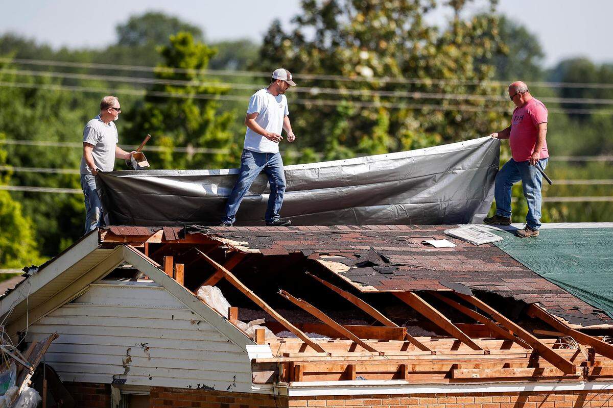 Chris Colier, left, with help from John McKinney, center, and another neighbor spread a tarp out to cover the roof on Sunday, May 18, 2025, at his house off U.S. Route 27 in Somerset, Ky. Colier said he was preparing for rain to fall on Monday.