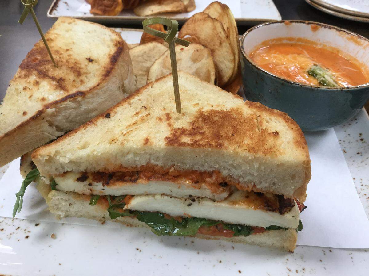 The grilled cheese sandwich is grilled marinated halloumi cheese, with arugula, and roasted red pepper, kalamata, lemon aioli on thick buttery white bread. It’s served with a cup of tomato soup and housemade chips.