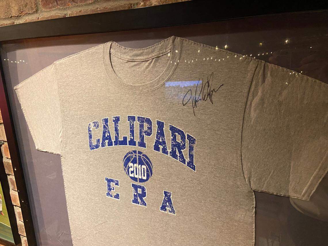 A framed “Calipari Era” T-shirt from 2010 featuring a signature on it from John Calipari hangs in the stairway of Jack Demsey’s in New York City. The establishment of the bar and restaurant as the home base for the New York City UK Alumni Club coincided with Calipari’s arrival at Kentucky.