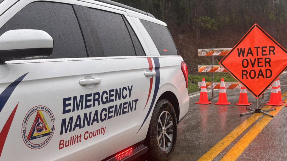 Photo of an emergency vehicle with its lights on in front of a road sign blocking cars from entering a flooded road.