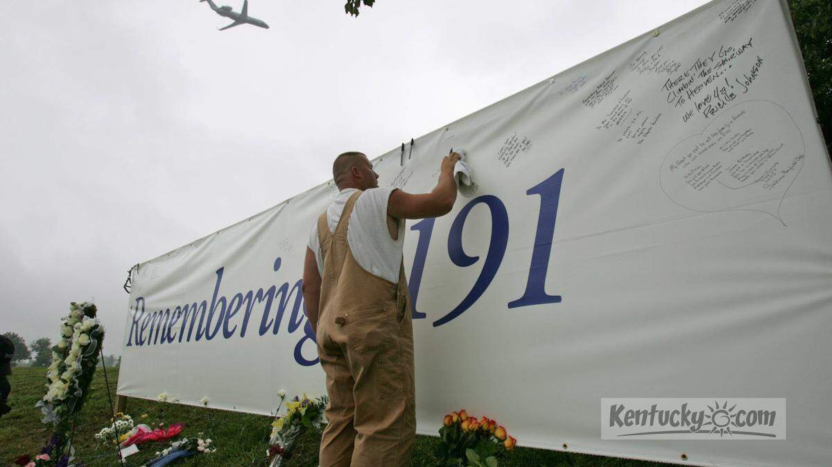 As a jet takes off overhead, Coy Chilton, Salvisa, Ky., wrote a note on the sign at the Flight 5191 Memorial that has been set up in front of the Blue Grass Airport on Versailles Rd. in Lexington,Ky., Wednesday, August 30, 2006. Comair Flight 5191 crashed  on takeoff Sunday morning at Blue Grass Airport killing 49 people. He knew Bobby Meaux who was killed in the crash. Charles Bertram/Staff.   Keyword: Delta Comair  Flight 5191 plane crash