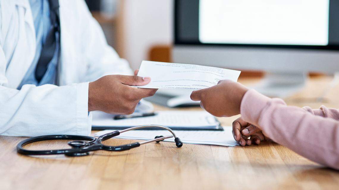 In this stock photo, we see a closeup shot of an unrecognizable doctor giving paperwork to a patient during a consultation