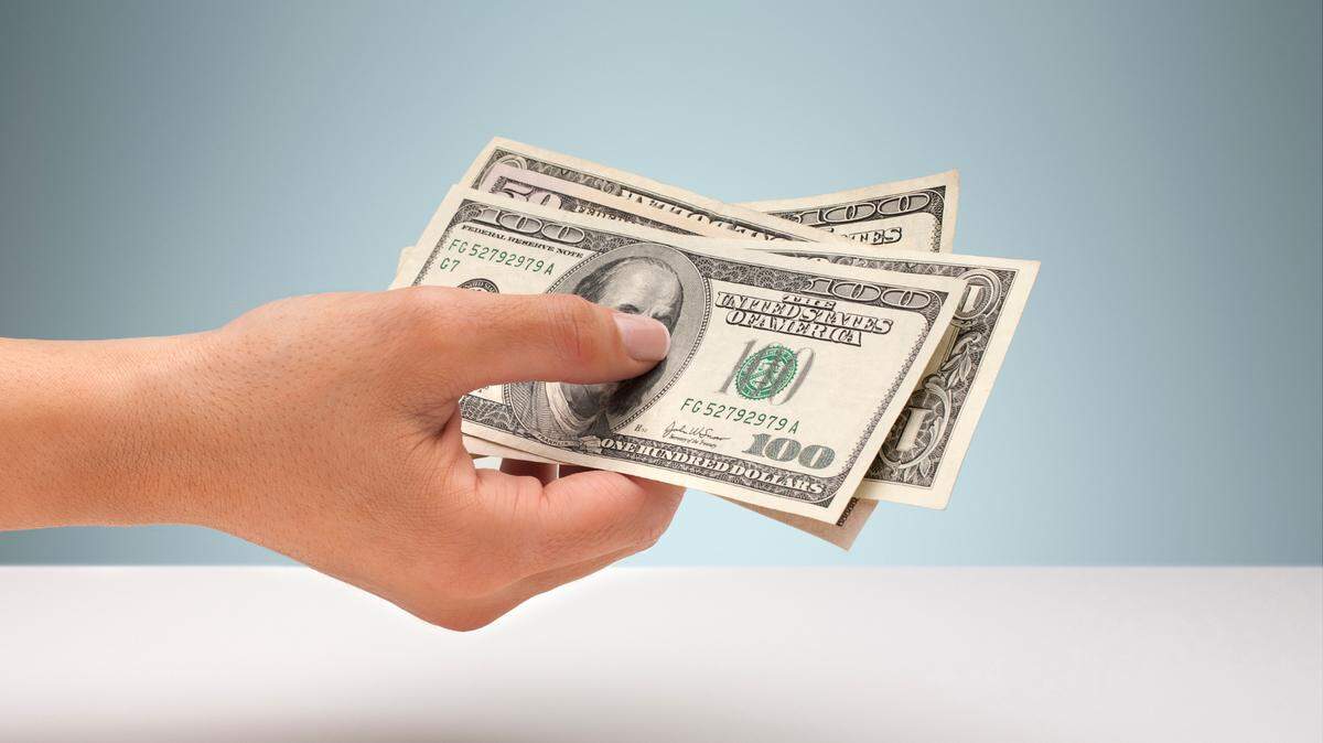 A hand holds some cash, including several $100 bills.