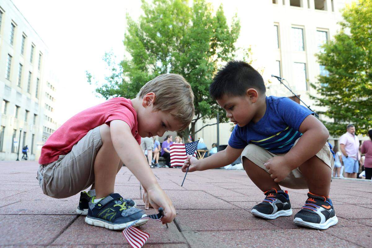 Isaiah Howard, 3, left, and Abel Banderas, 2, played with U. S. flags Friday evening during Lights For Liberty: A Vigil to End Human Detention Camps at Courthouse Plaza in Lexington.
