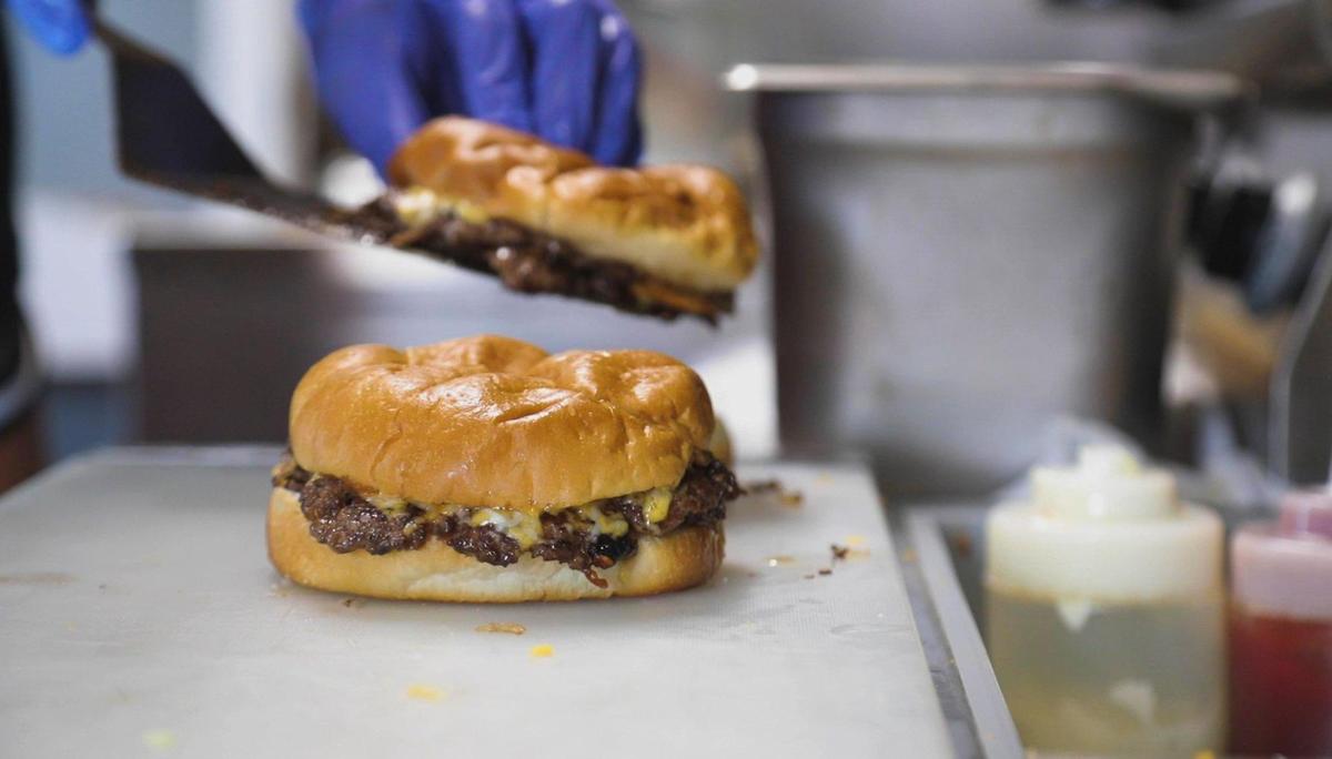 Assistant manager Laken Burchett prepares a Big T Burger at the Drive-In restaurant in Olive Hill. It features three two-ounce beef patties. The burger has become a competitive endeavor with patrons seeing who could eat the biggest Big T ​ — the current record stands at a burger with 21 patties.