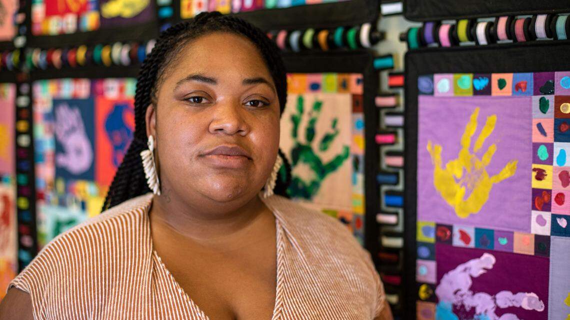 Chantal Hughes stands in front of the quilted art piece hanging in the Health Access Nurturing Development Services section of the Lexington Family Care Center on June 1, 2021.