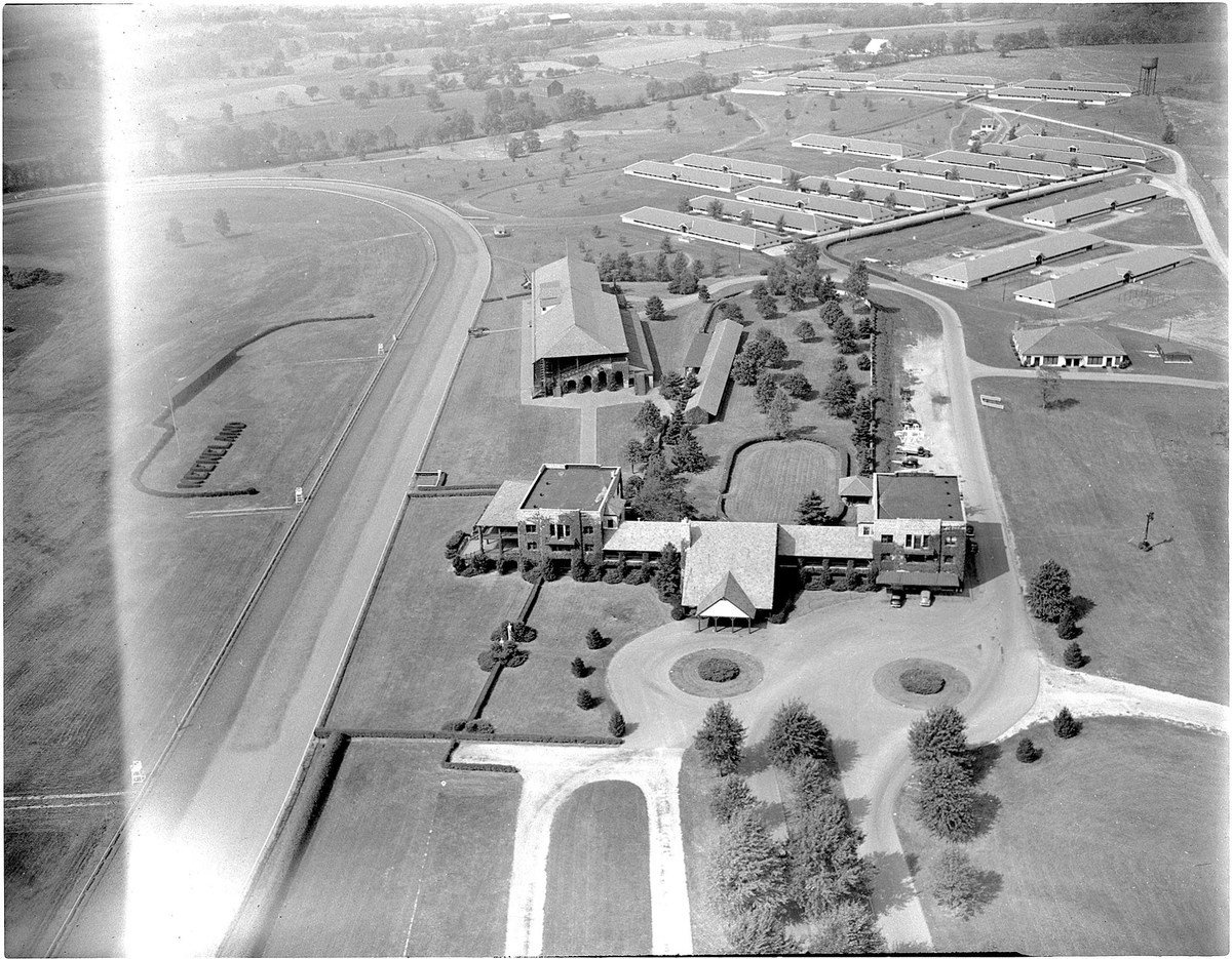 The Herald-Leader photographer snapped this aerial photograph of the Keeneland race course October 4, 1947. In the foreground is the spacious clubhouse while the grandstand is shown in the center of the picture. To the right of the grandstand may be seen Keeneland’s famous open-air paddock while some of the stables are shown at top right. The home stretch, the first turn and a portion of the Keeneland infield, where the totalisator board will be erected, are at the left. At lower left is part of the clubhouse parking lot.