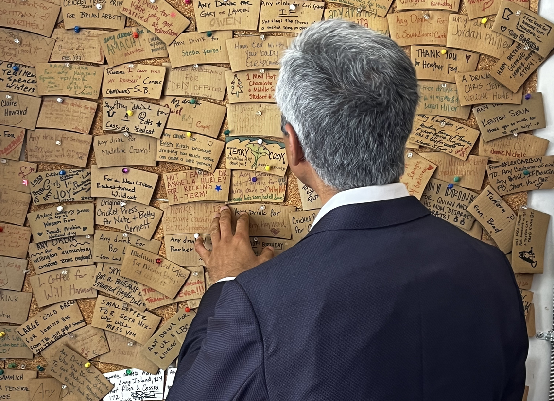 Former U.S. Surgeon General Vivek Murthy looks at the pay-it-foward board at A Cup of Commonwealth.