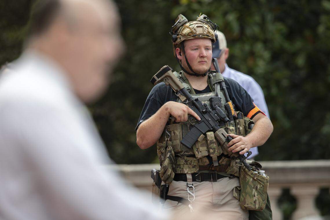 A man with a rifle stands by as Kentucky Freedom Rally organizer Lee Watts speaks during the rally at the state Capitol in Frankfort, Ky., on Saturday, May 2, 2020.