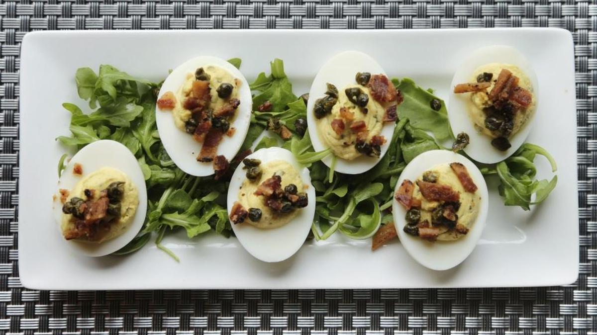 Deviled eggs made with smoked salmon, bacon bits, fried capers and served on a bed of arugula.