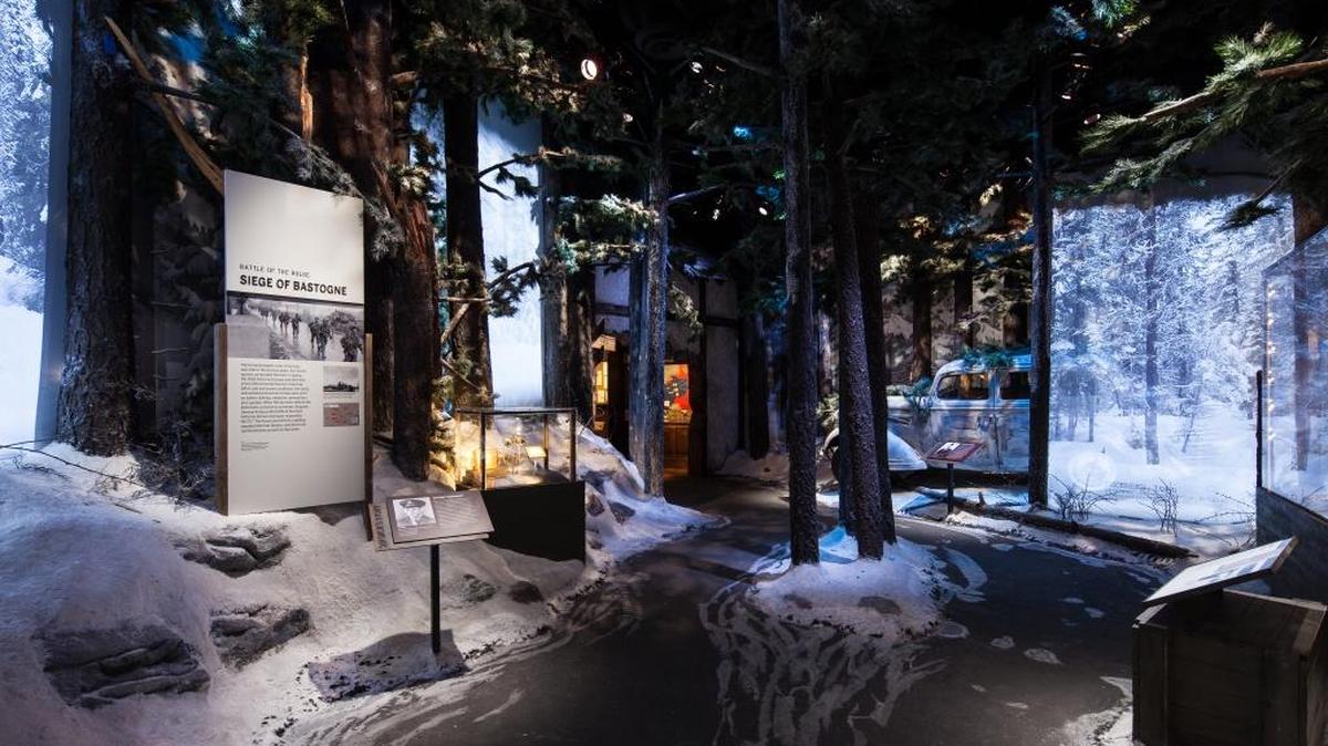 The Battle of the Bulge gallery within The National WWII Museum's Road to Berlin: European Theater Galleries immerses visitors in the frozen Ardennes forest, where citizen soldiers—caught off guard and without proper winter gear—defended their battered line against Hitler’s final surge. A large-scale dimensional video (left) and running audio of German and American voices evokes the chaos and danger of this costly battle, as visitors walk through the recreated forest toward a camouflaged Opel staff car, abandoned by the German army.