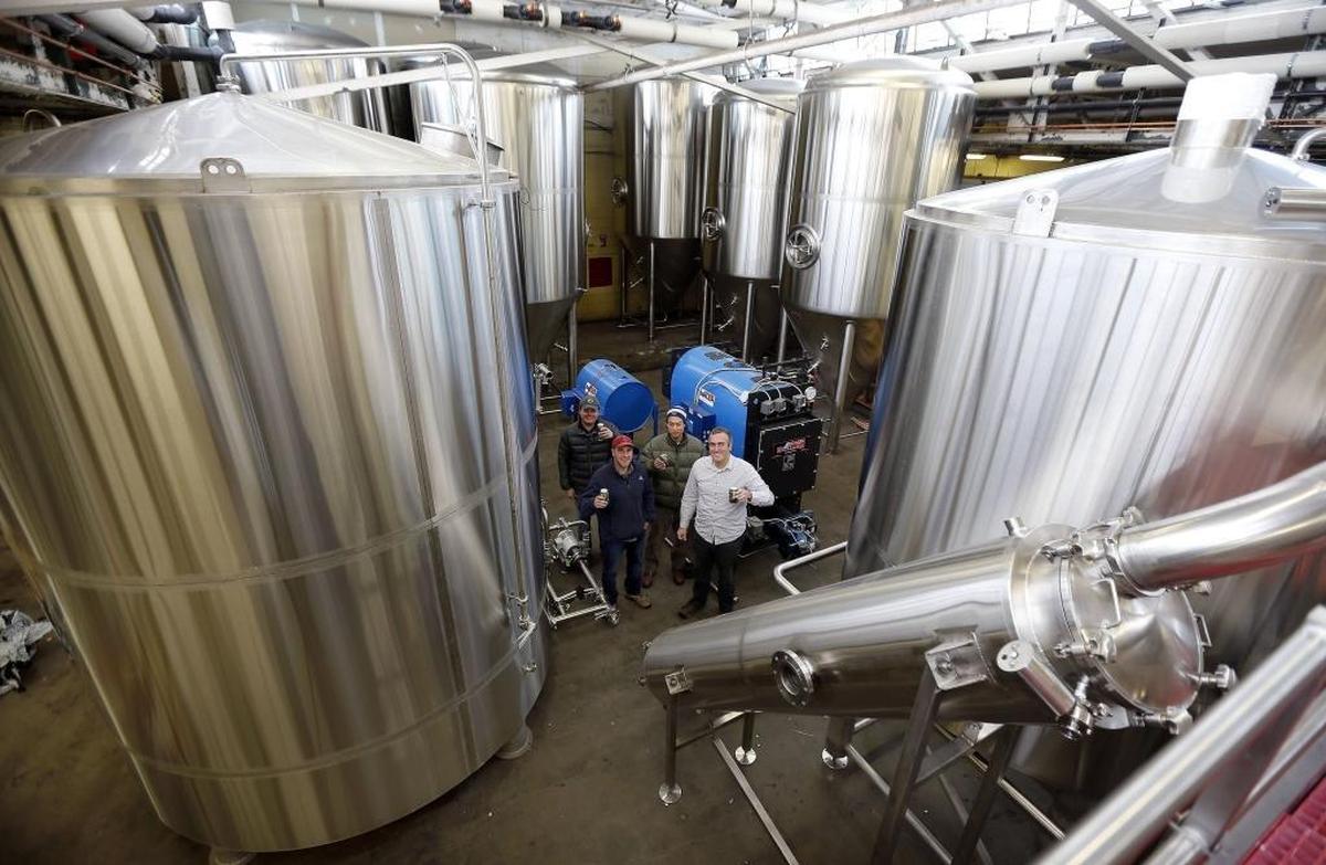 West Sixth Brewery founders, left to right, Brady Barlow, Joe Kuosman, Robin Sither and Ben Self posed by new fermenters and liquor tanks in 2014 during their first big expansion. The founders think their company’s growth during its first five years has been fueled in part by community engagement, philanthropy and generosity to employees.