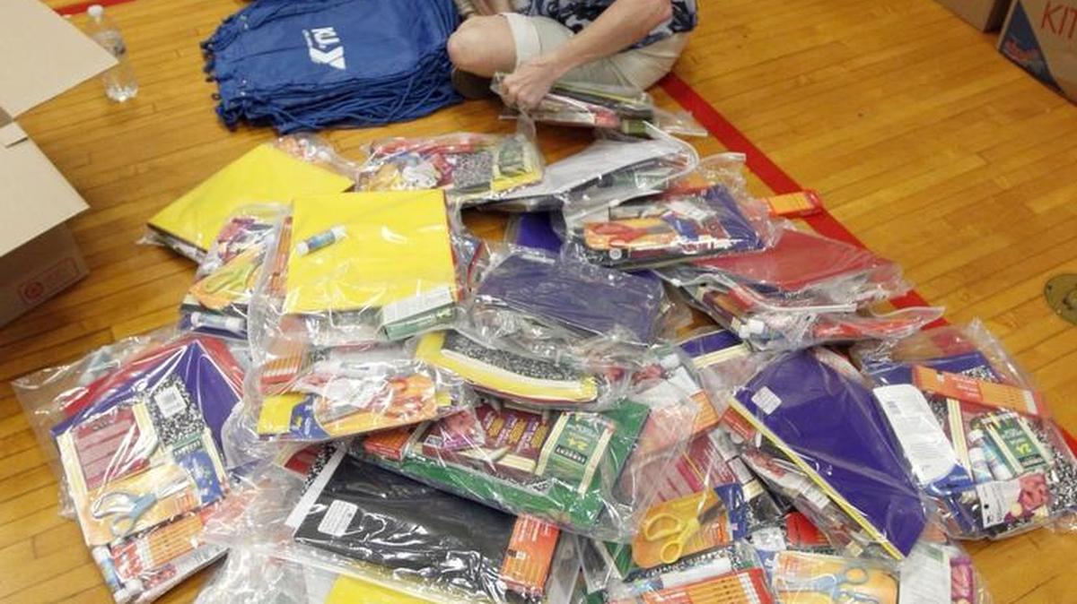 Volunteer Debbie King filled backpacks in 2013 for YMCA back-to-school rallies. This year’s rallies will take place at noon Saturday.