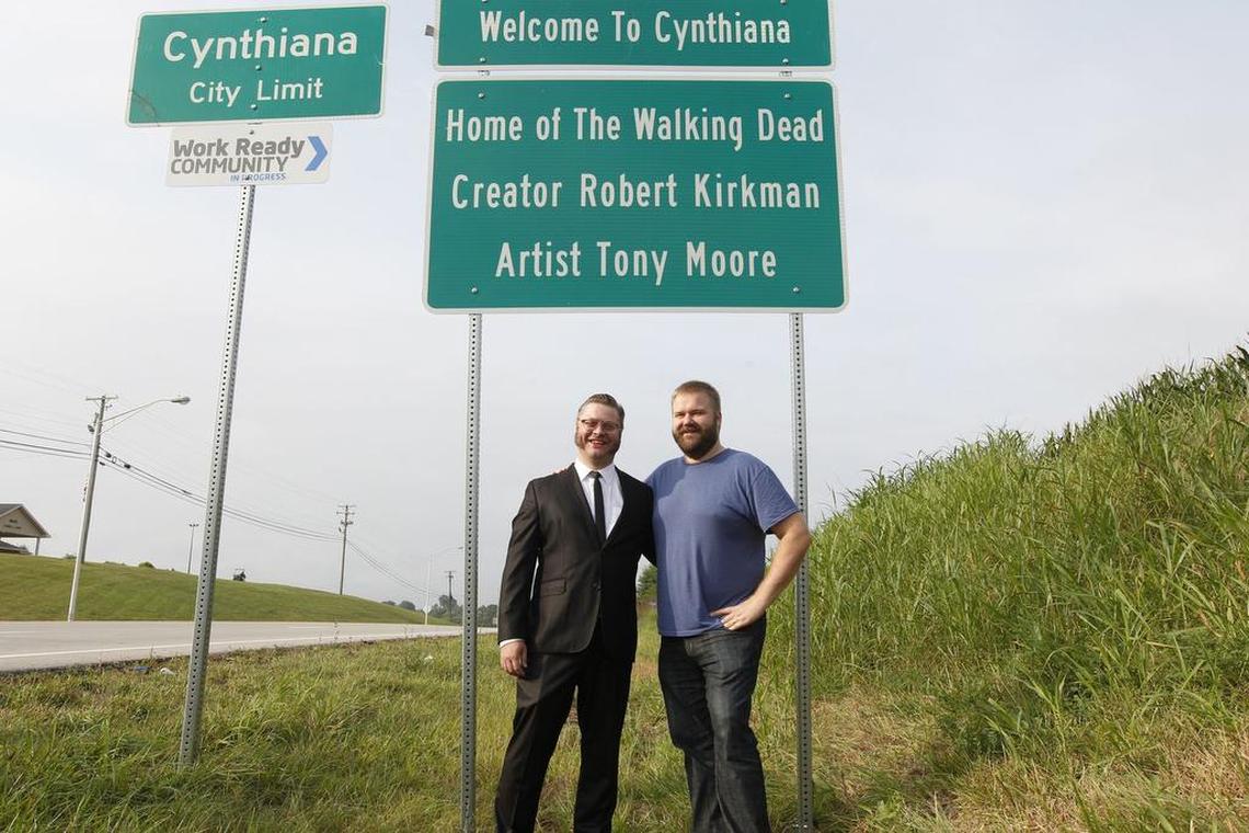 Comic book writer Robert Kirkman and artist Tony Moore, creators of The Walking Dead, stand in front the Cynthiana, Ky., welcome sign that includes their names.